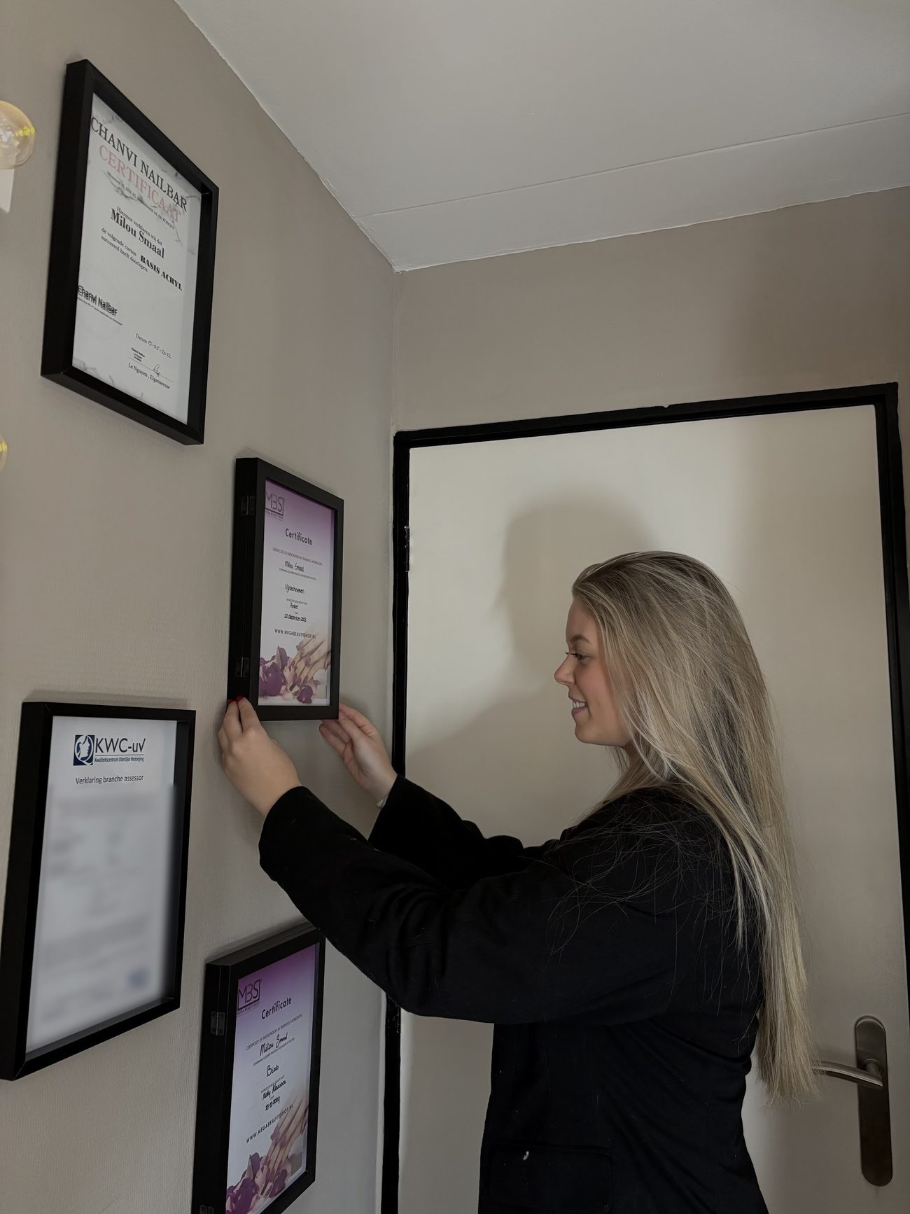 Milou hangt haar ingelijste certificaten op aan de muur van haar studio