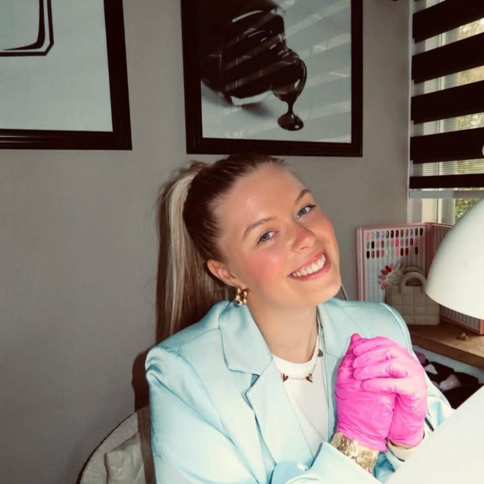 Milou lacht, in een lichtblauwe blazer met roze handschoenen aan haar tafel