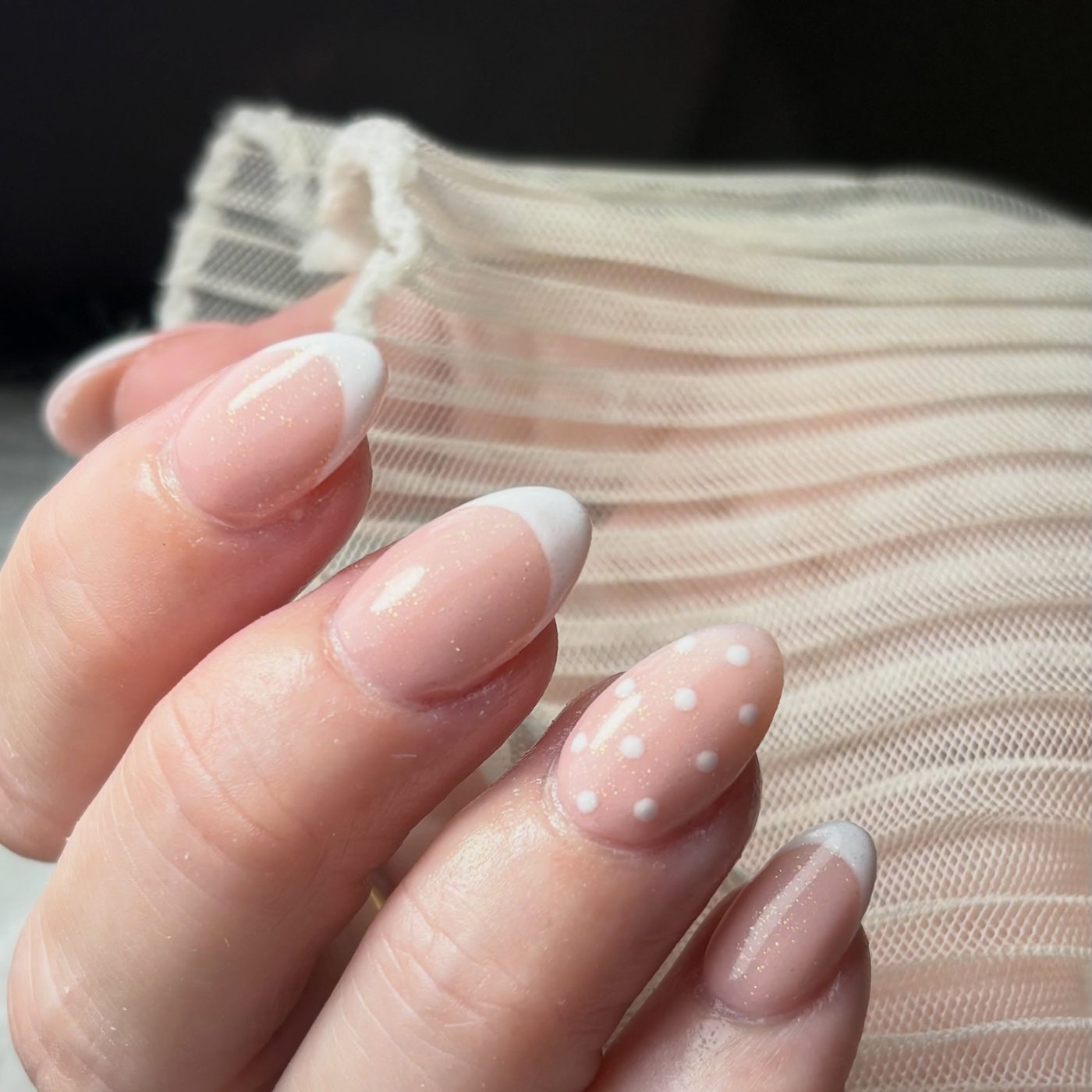 Nude nagels met een witte french en één nagel met stipjes